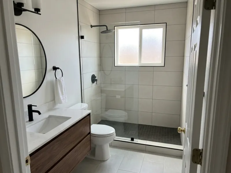 Finished bathroom: walk-in tile shower with a glass panel and matte black fixtures, floating walnut vanity with a white quartz top, light gray porcelain floor.